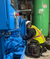 compressed-air-expert-wearing-a-yellow-high-visibility-vest-while-working-on-a-blue-K-Series-oil-lubricated-rotary-screw-air-compressor-at-a-chemical-manufacturing-plant