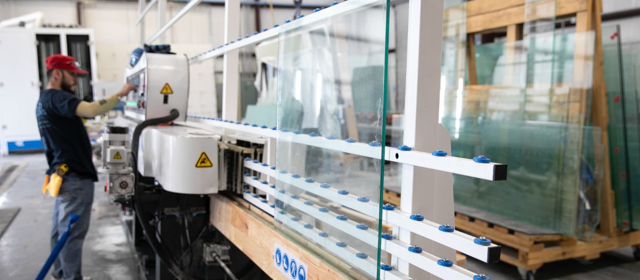 A man operates a glass cutting machine in a factory