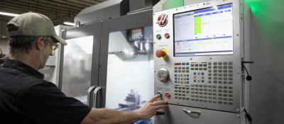 a man in a hat presses buttons on a CNC machine