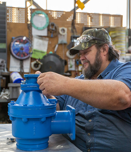 Rogers-Machinery-service-expert-wearing-blue-repairing-a-blue-inlet-valve-for-a-customer