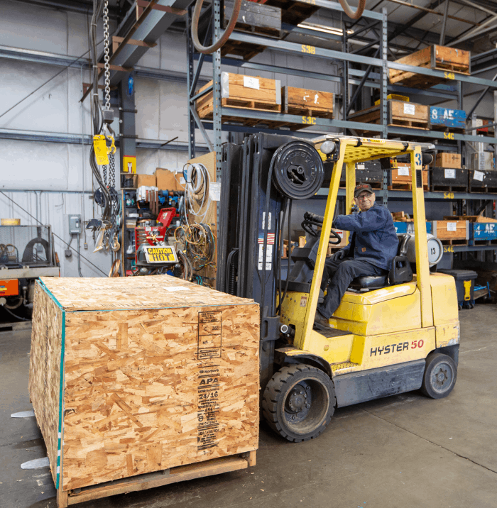 man-drivng-a-yellow-forklift-that-is-carrying-a-wooden-box-a-vacuum-pump-inside-at-Rogers-Machinery-Company-repair-warehouse