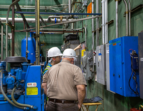 Rogers-Machinery-compressed-air-audit-expert-wearing-a-white-hard-hat-talking-to-a-food-production-facilities-manager-while-discussing-energy-saving-air-system-reccomendations