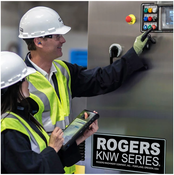 a man and a woman in safety gear check out a compressor. The woman holds a tablet and the man points to controls